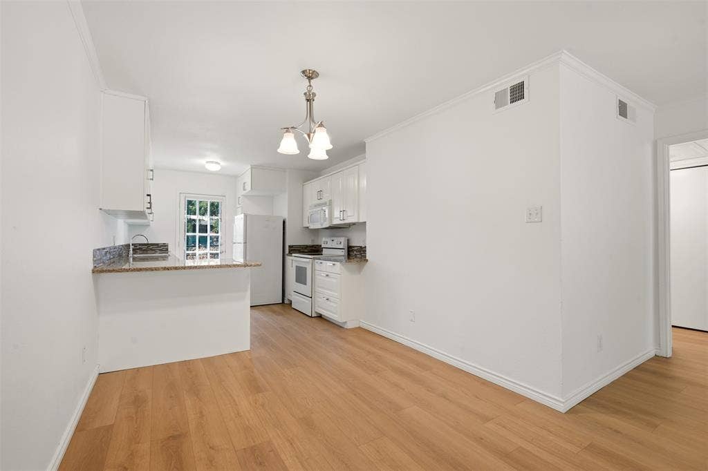 Kitchen featuring white cabinetry, light granite-style countertops, wood-finish flooring, a mosaic tile backsplash, and a white appliance package