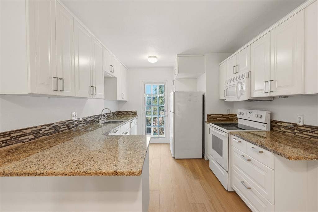 Kitchen featuring white cabinetry, light granite-style countertops, wood-finish flooring, a mosaic tile backsplash, and a white appliance package