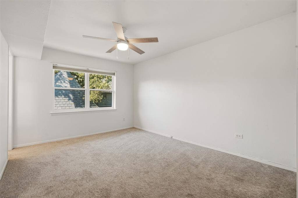 Carpeted flooring, white painted walls, white trim, window with roller shade, and a ceiling fan with integrated lighting