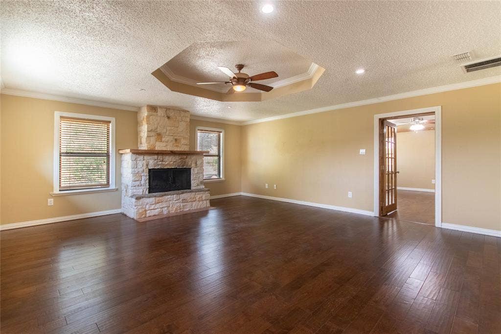 Wood-finish flooring, stone-clad fireplace with wood mantle, recessed lighting, ceiling fan, and tray ceiling