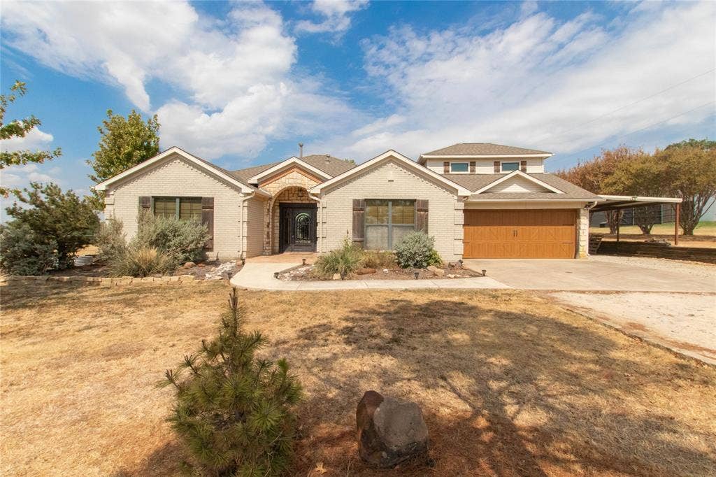 Stucco exterior with stone accents, arched entryway, two-car garage with wood-finish door, and an attached carport