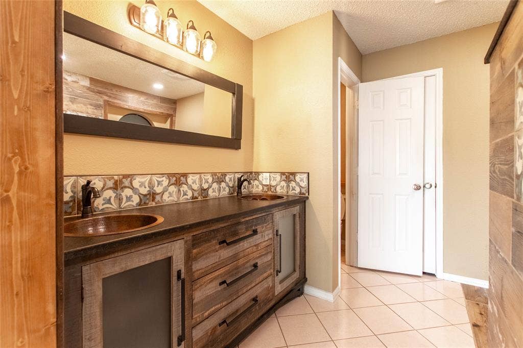 Wood-finish vanity with dual copper vessel sinks, patterned tile backsplash, and a contemporary light fixture