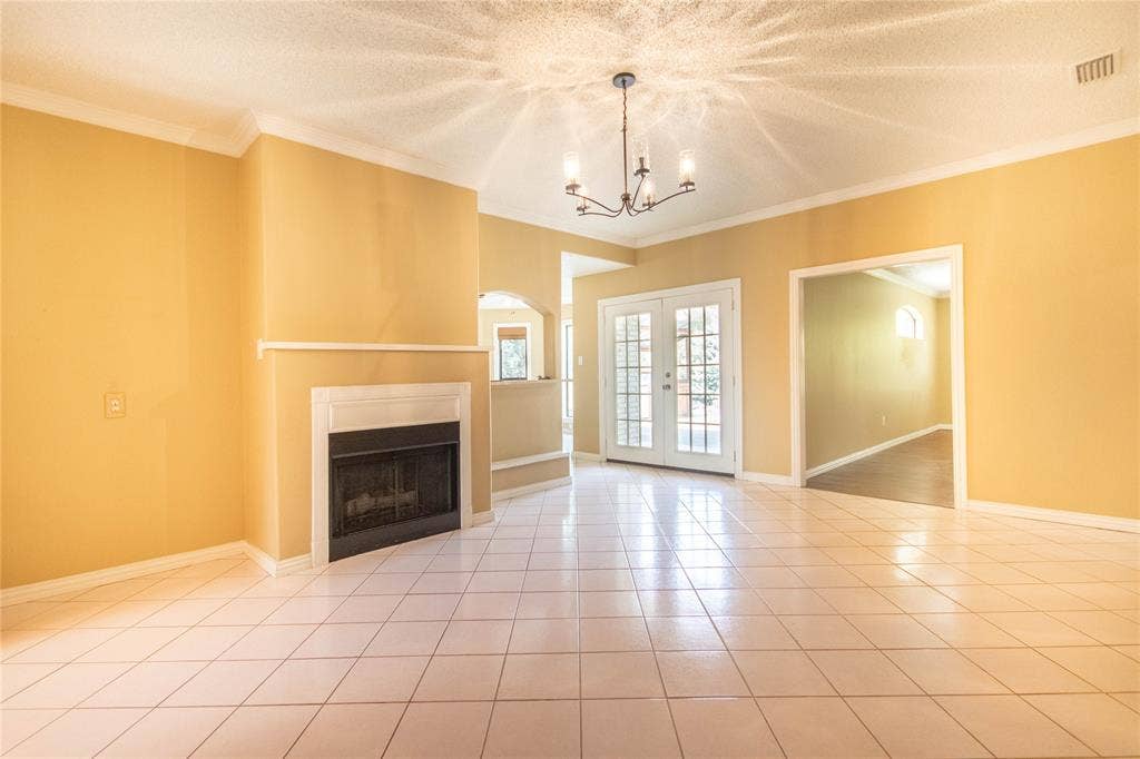 Tile flooring, crown molding, double French doors, fireplace with mantel, and a multi-arm chandelier