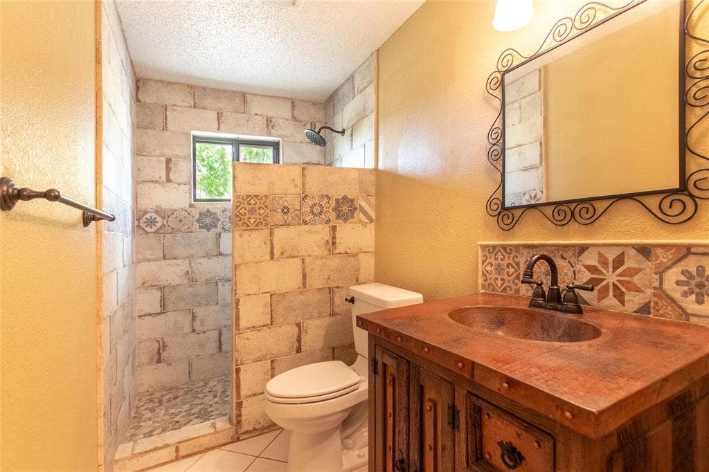 Custom vanity with an integrated copper sink, decorative tile backsplash, and a framed wall mirror