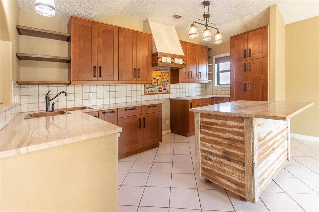 Kitchen featuring wood cabinetry, light-toned countertops, white tiled backsplash, and a central island with a stone-finish top