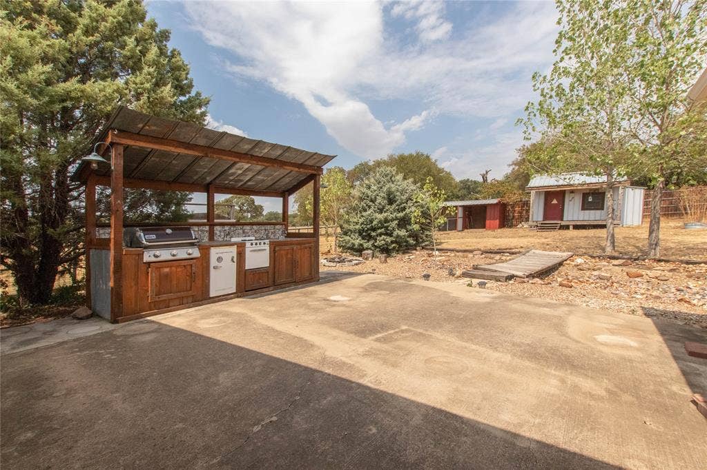 Outdoor kitchen featuring a built-in grill, sink, and wood cabinetry with a metal roof