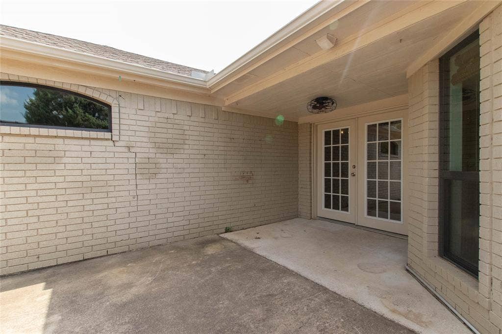 Covered patio area with concrete flooring, brick exterior, and French doors