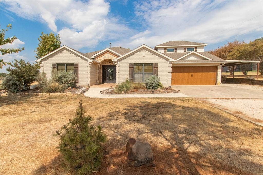 Stucco exterior with stone accents, attached garage with wood-finish door, and a covered side carport