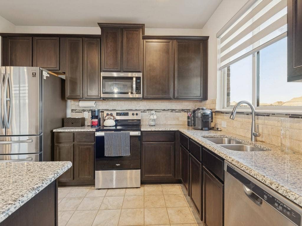 3825 S Courtney Court, Heartland, TX 75126 Dark wood-finish cabinetry with crown molding, stainless steel appliances, granite countertops, tile backsplash, and a double basin stainless steel sink