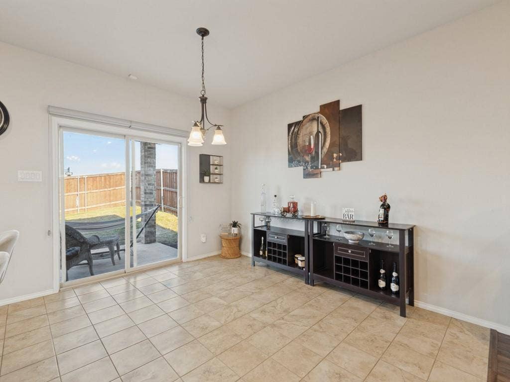 3825 S Courtney Court, Heartland, TX 75126 Porcelain tile flooring, sliding glass patio door, outdoor patio, backyard with privacy fencing, and a chandelier-style ceiling fixture