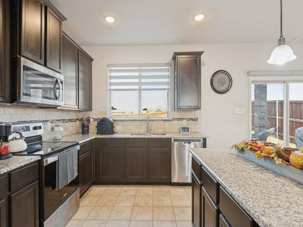 3825 S Courtney Court, Heartland, TX 75126 Modern kitchen featuring dark wood cabinetry, stainless steel appliances, and granite countertops with waterfall edge