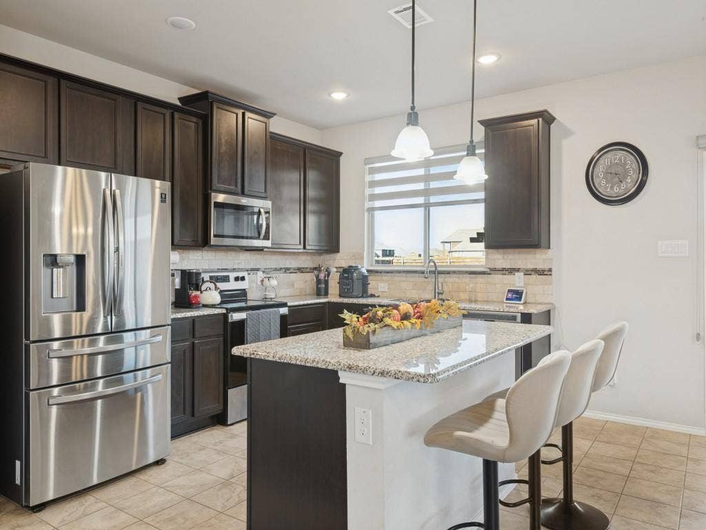 3825 S Courtney Court, Heartland, TX 75126 Kitchen featuring dark wood-finish cabinetry, stainless steel appliances, granite countertops, an undermount sink, and a tiled backsplash