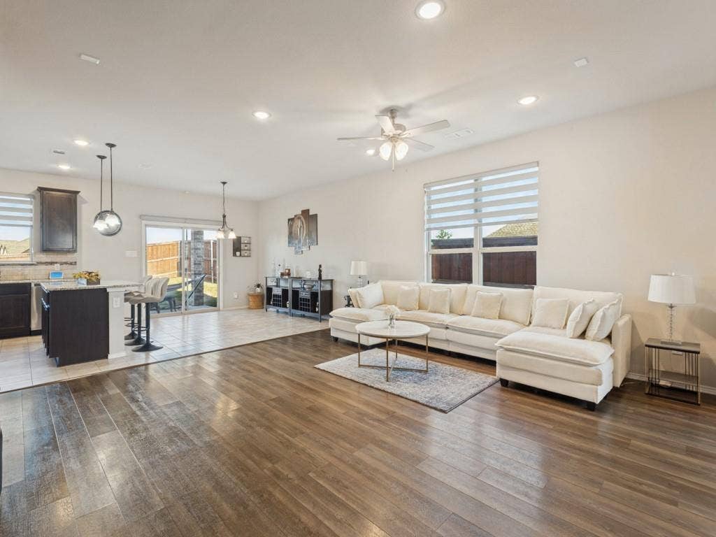 3825 S Courtney Court, Heartland, TX 75126 Open-concept living area featuring warm wood-finish flooring throughout, a spacious sectional layout, recessed ceiling lighting, and ceiling fan with integrated light fixture