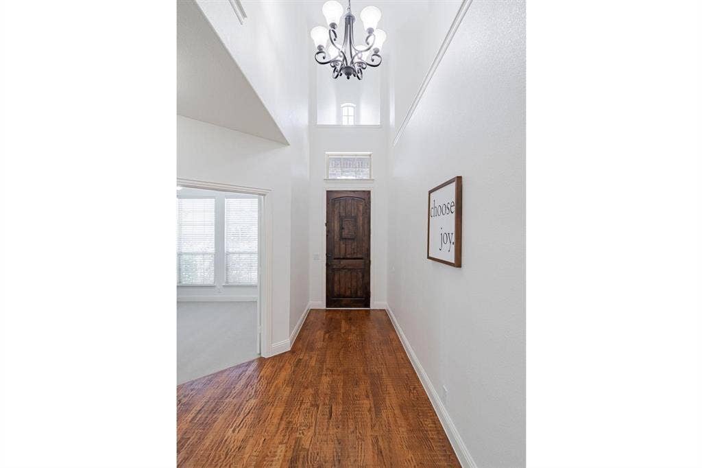 Vaulted entryway featuring a decorative chandelier, rich wood-finish flooring, and a carved wood entry door with transom window