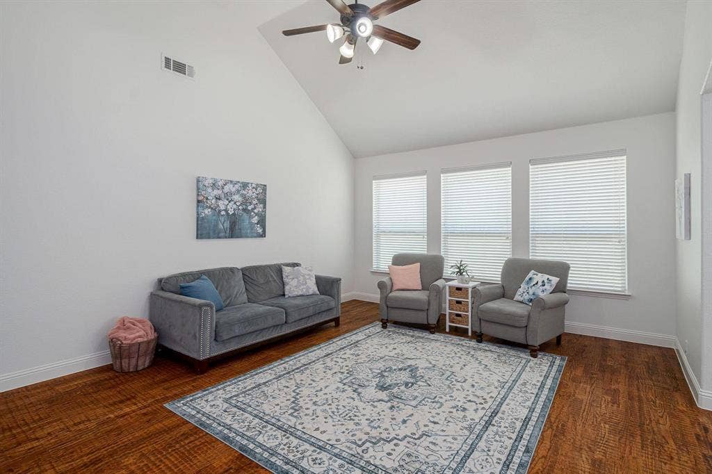 Vaulted ceilings with a ceiling fan, three windows with blinds, and wood-finish flooring