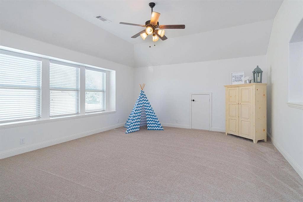 Vaulted ceiling with a ceiling fan, carpeted flooring, multiple windows, and a built-in arched alcove
