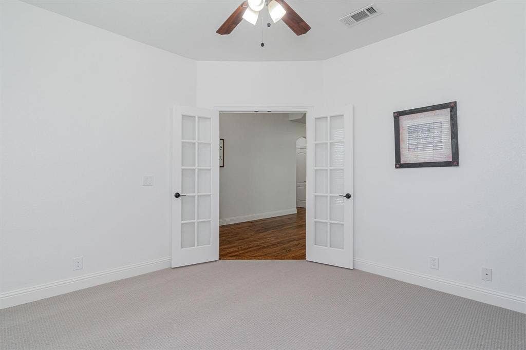 Light-colored carpeting with white baseboards, a ceiling fan with light fixture, and French doors