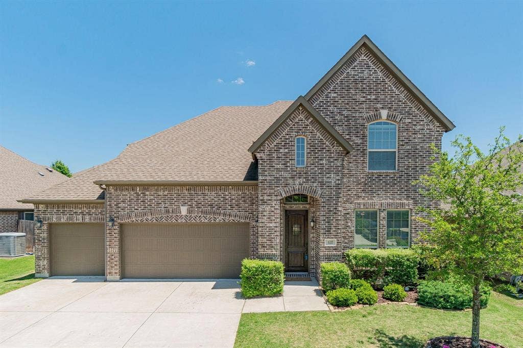 Brick exterior with an arched entryway, two-car garage, and established landscaping