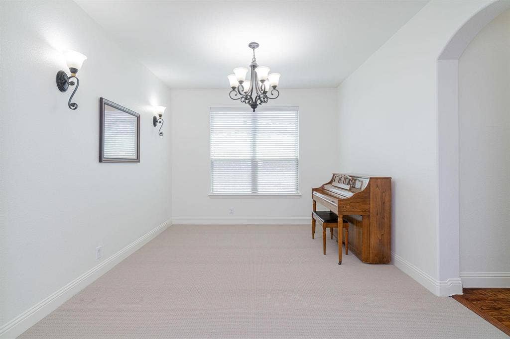 Recessed window with blinds, wrought iron chandelier, wall sconces, arched doorway, and carpeted flooring