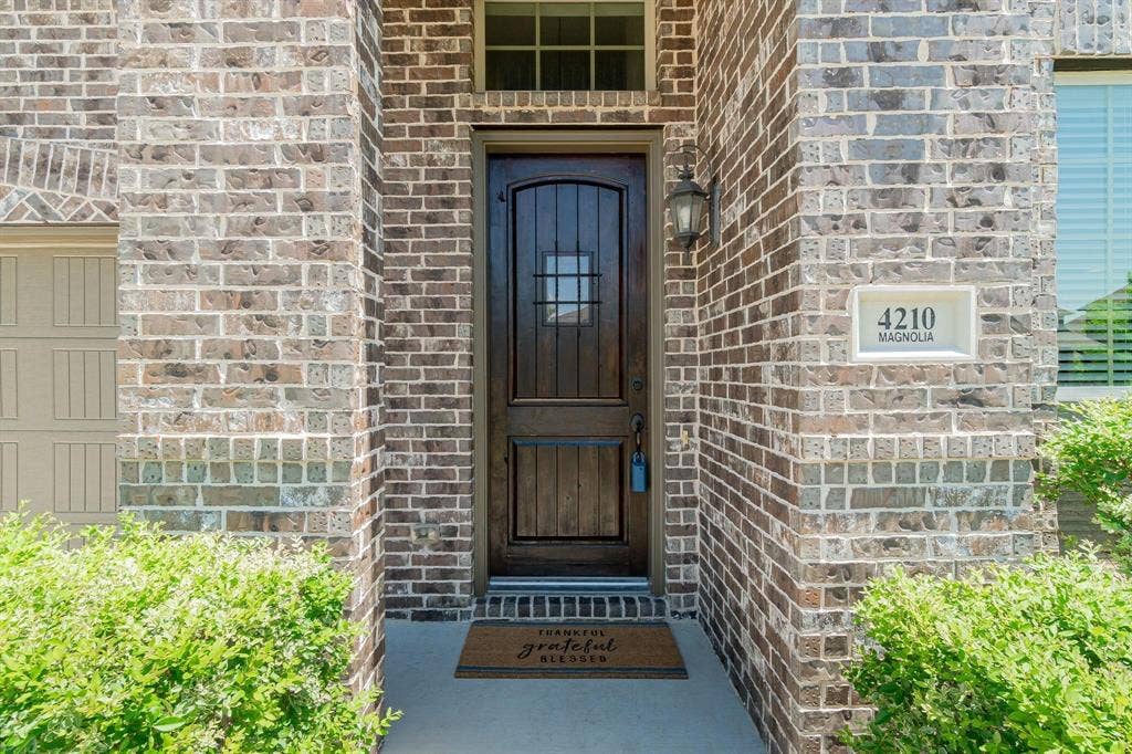 Brick exterior with an arched entryway, featuring a dark wood door with glass inserts and an exterior wall lantern