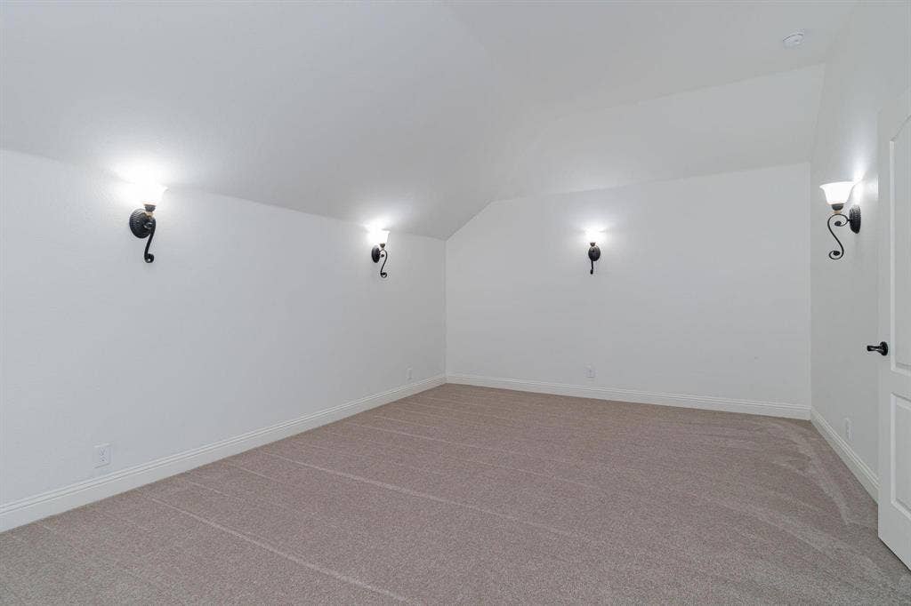 Sloped ceiling room featuring carpet flooring, crisp white walls, and decorative wall sconces