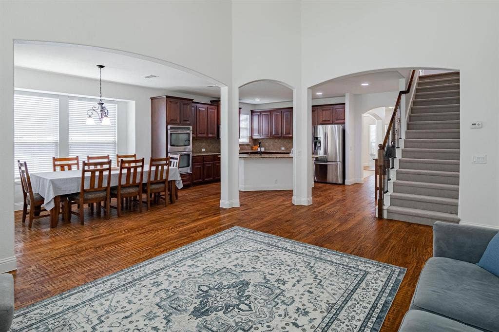 Arched doorways, wood-finish flooring, staircase with carpeted treads, dark wood cabinetry, and stainless steel appliances