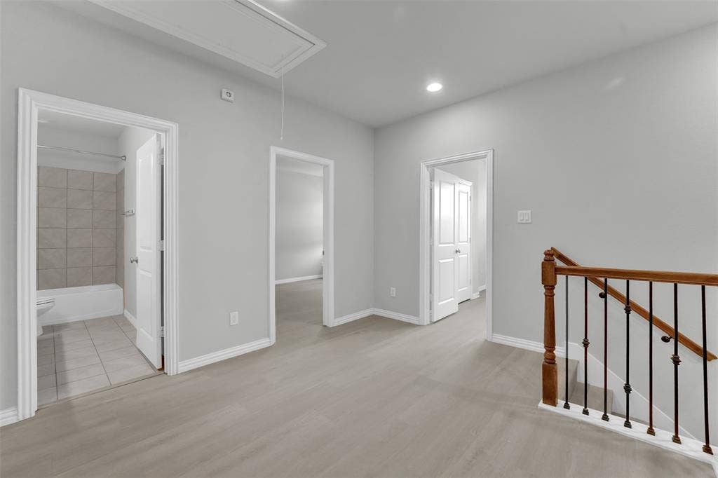 8266 Primrose Way, Dallas, TX 75252 Light gray wood-finish flooring, recessed lighting, white trim, and a staircase with wood handrails and black metal balusters