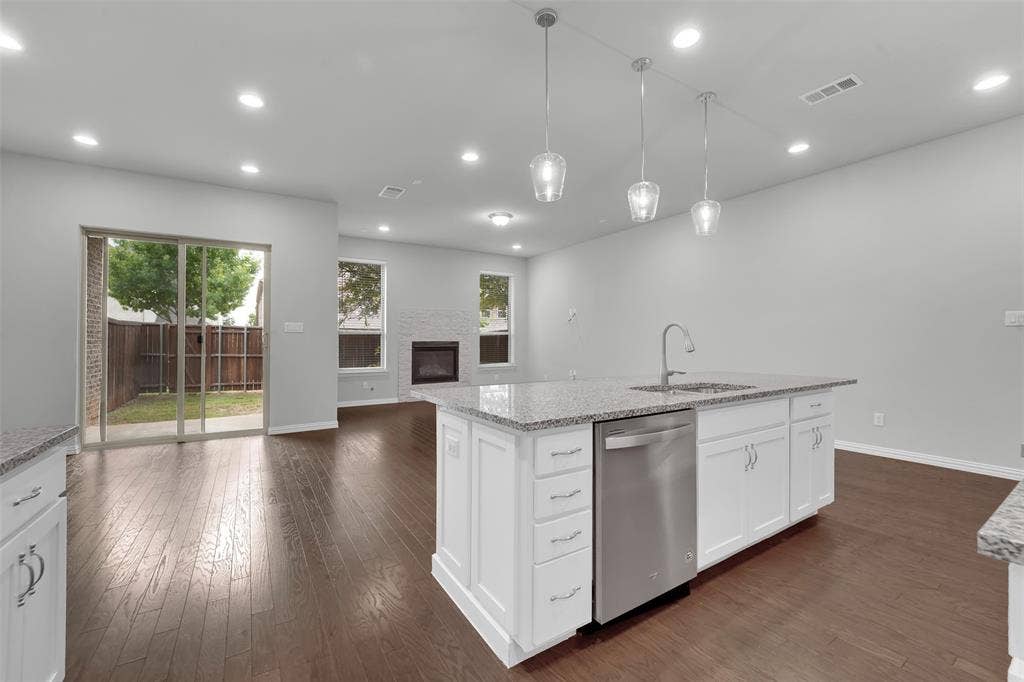 8266 Primrose Way, Dallas, TX 75252 Open-concept living space with dark wood-finish flooring, white shaker cabinetry, an island with a stainless steel sink and dishwasher, and recessed lighting