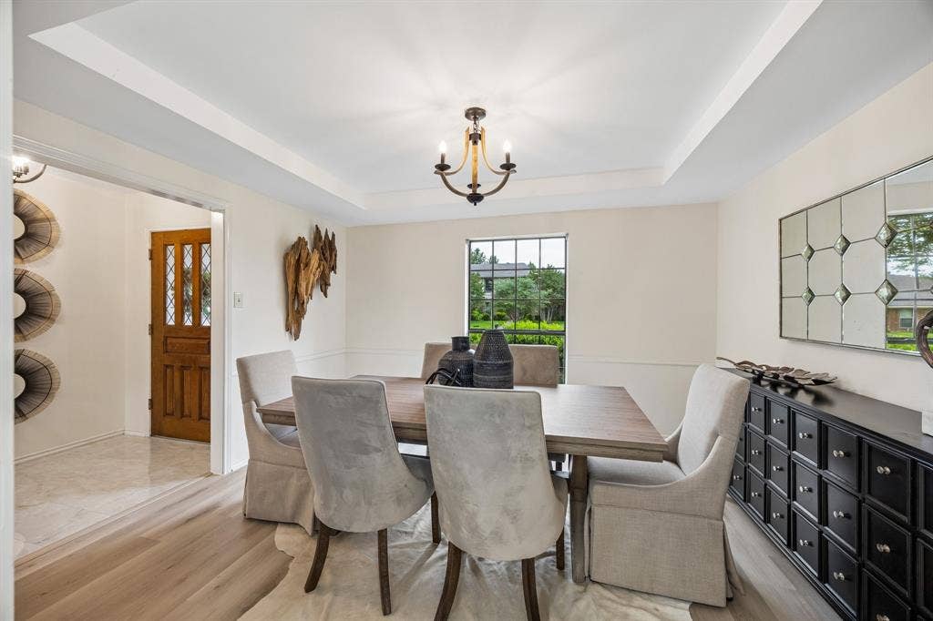 4540 New Orleans Drive, Plano, TX 75093 Tray ceiling with a chandelier, wood-finish flooring, white wall paneling, and a large window