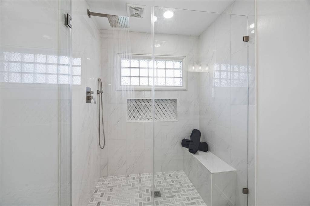 4540 New Orleans Drive, Plano, TX 75093 Glass-enclosed shower with a rainfall showerhead, integrated bench, recessed shelving with decorative tile, and a glass block window