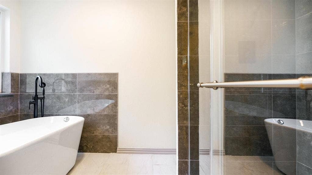 2616 Ellis Court, Plano, TX 75075 Freestanding soaking tub with a floor-mounted black faucet, glass-enclosed shower, and large format wall tiling