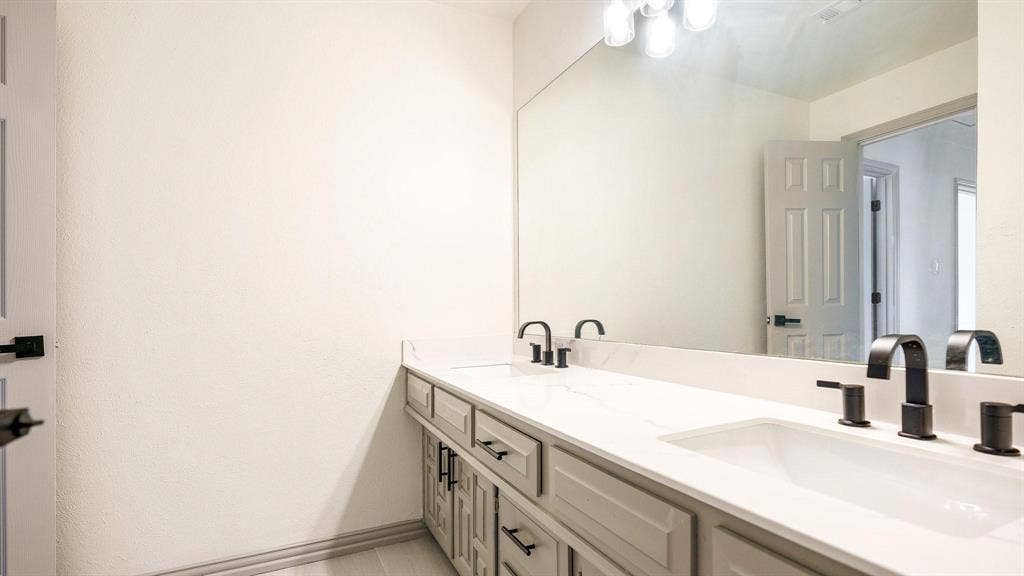 2616 Ellis Court, Plano, TX 75075 Dual undermount sinks with matte black fixtures, an expansive vanity mirror, light-toned cabinetry with dark hardware, and a stone-finish countertop