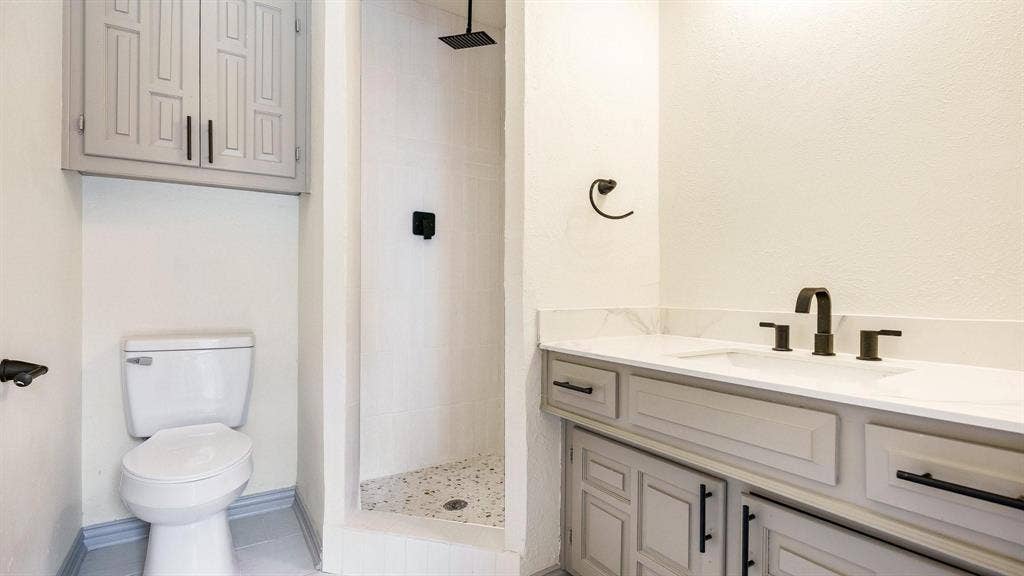 2616 Ellis Court, Plano, TX 75075 Walk-in shower with tiled walls and floor, dual vanity with light-toned cabinetry, white countertop, and dark-toned hardware, and an overhead built-in storage cabinet