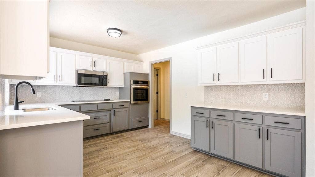 2616 Ellis Court, Plano, TX 75075 Two-tone cabinetry with matte black hardware, stainless steel appliances, light-toned countertops, tile backsplash, and wood-finish flooring