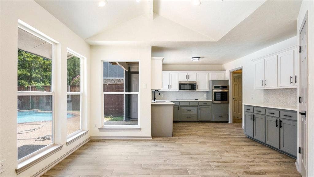2616 Ellis Court, Plano, TX 75075 Wood-finish flooring, vaulted ceiling, two-tone cabinetry, stainless steel appliances, and a visible pool