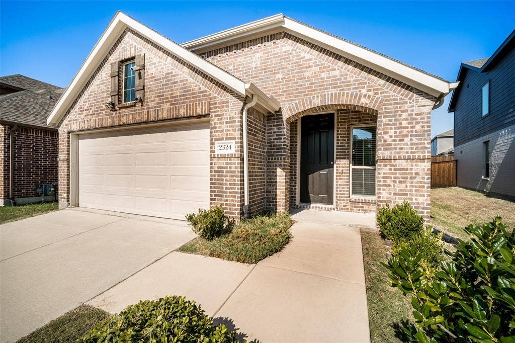 2324 Neff Lane, Forney, TX 75126 Brick exterior featuring a gabled roofline, recessed arched entryway, two-car garage, and low-maintenance landscaping
