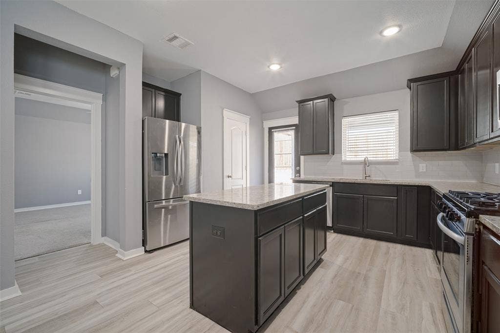 2324 Neff Lane, Forney, TX 75126 Kitchen featuring dark cabinetry, stone-surface countertops, central island, stainless steel appliances, and wood-finish flooring