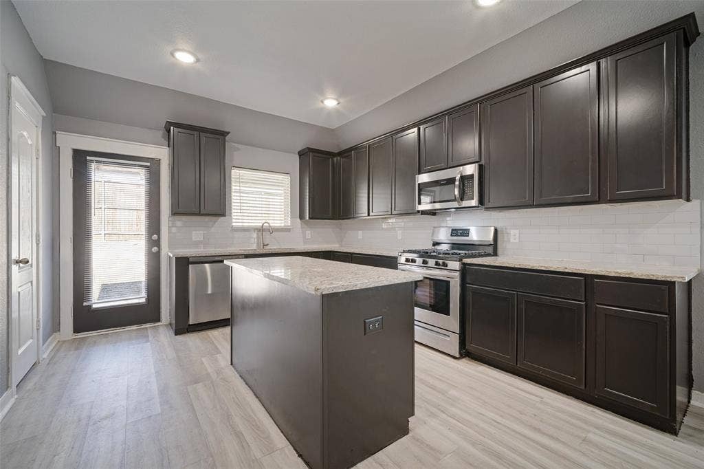 2324 Neff Lane, Forney, TX 75126 Kitchen featuring dark-finish cabinetry, light-toned stone-style countertops, white subway tile backsplash, stainless steel appliances, and wood-finish flooring