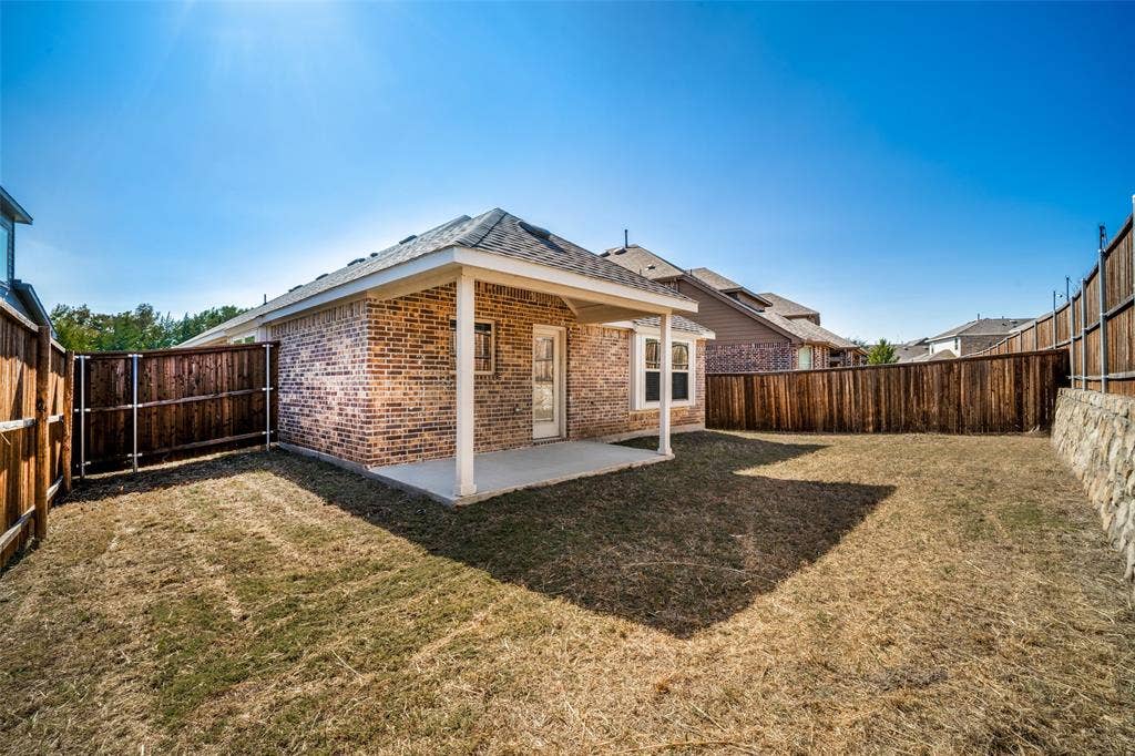 2324 Neff Lane, Forney, TX 75126 Brick exterior featuring a covered patio, concrete flooring, and surrounding wood privacy fencing with stone retaining wall elements