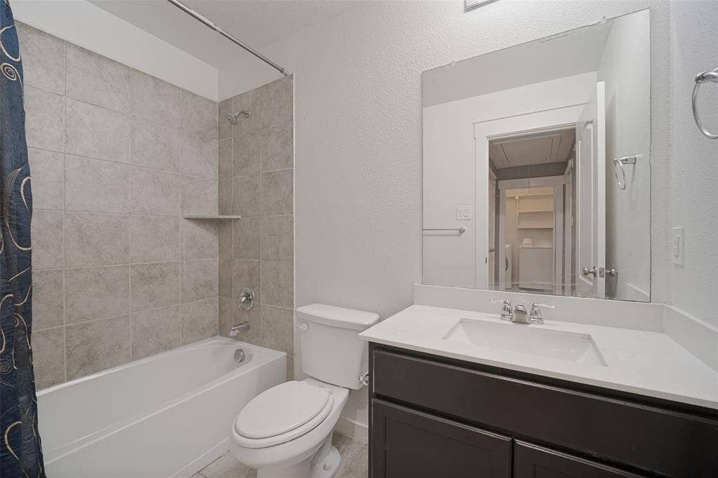 2324 Neff Lane, Forney, TX 75126 Bathroom featuring a vanity with a white countertop and rectangular undermount sink, dark-toned cabinetry, a full-width wall-mounted mirror, and a tub with large-format stone-style wall tile