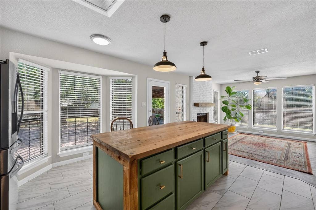519 Fox Creek Court, Denton, TX 76209 Kitchen island with wood-finish countertop and green cabinetry, bay window, white brick-finish fireplace, and ceiling fan