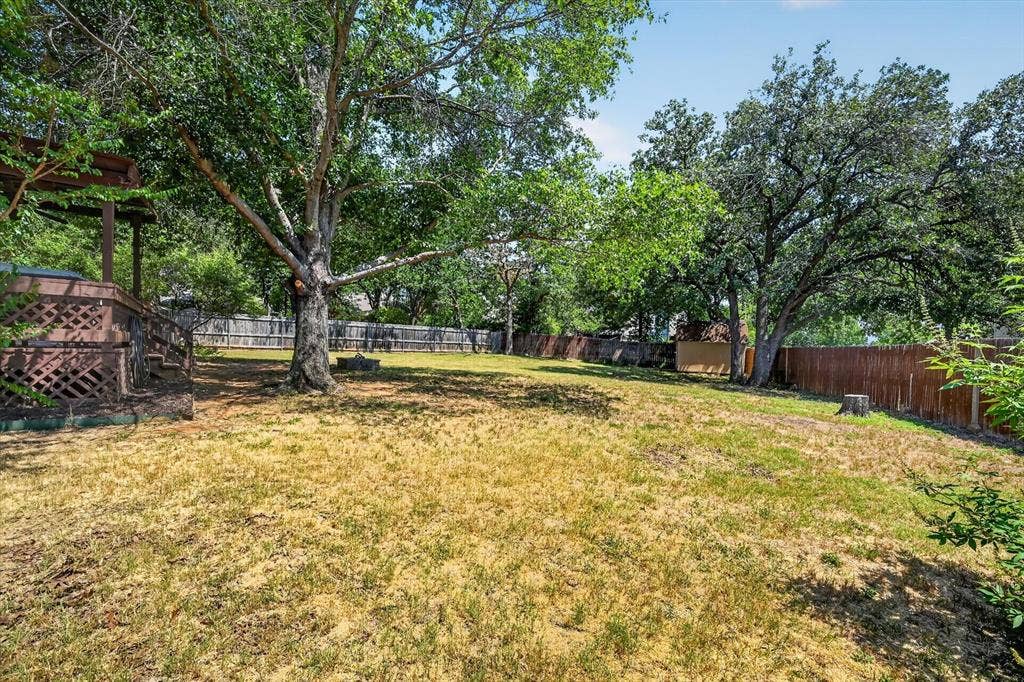 519 Fox Creek Court, Denton, TX 76209 Expansive backyard featuring a large mature tree, wood fencing, and a raised wood deck with lattice skirting