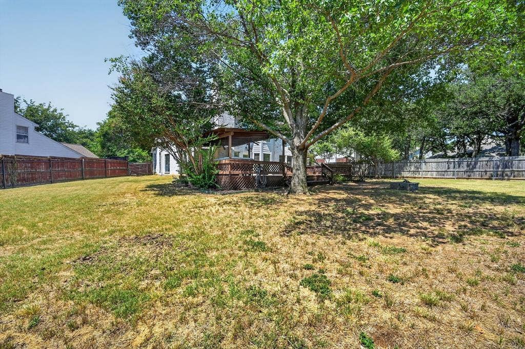 519 Fox Creek Court, Denton, TX 76209 Expansive backyard featuring a mature shade tree, a wood deck with lattice skirting, and a privacy fence
