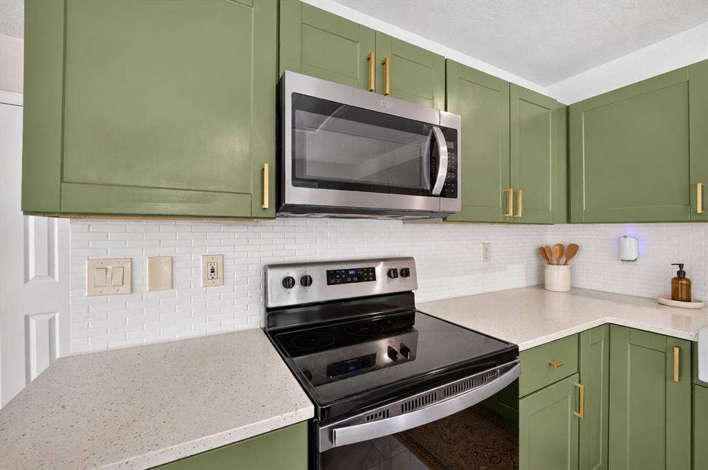 519 Fox Creek Court, Denton, TX 76209 Kitchen featuring sage green cabinetry with gold-tone hardware, stainless steel appliances, a white subway tile backsplash, and light-toned countertops