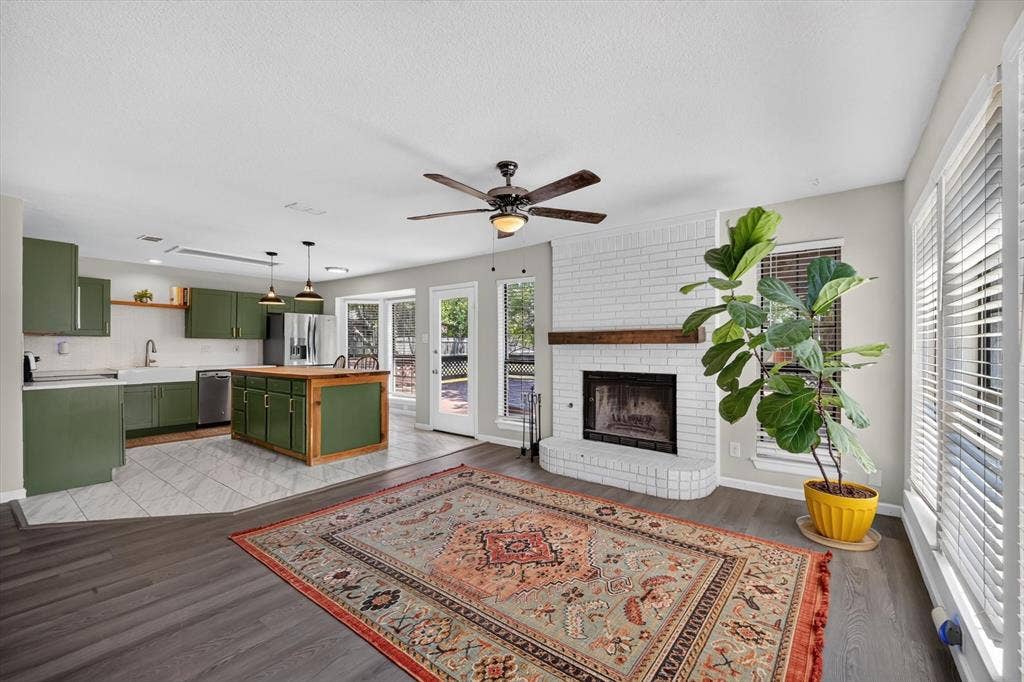 519 Fox Creek Court, Denton, TX 76209 Open-concept living space featuring a white brick fireplace with a wood-finish mantel, dark wood-finish flooring, and a ceiling fan