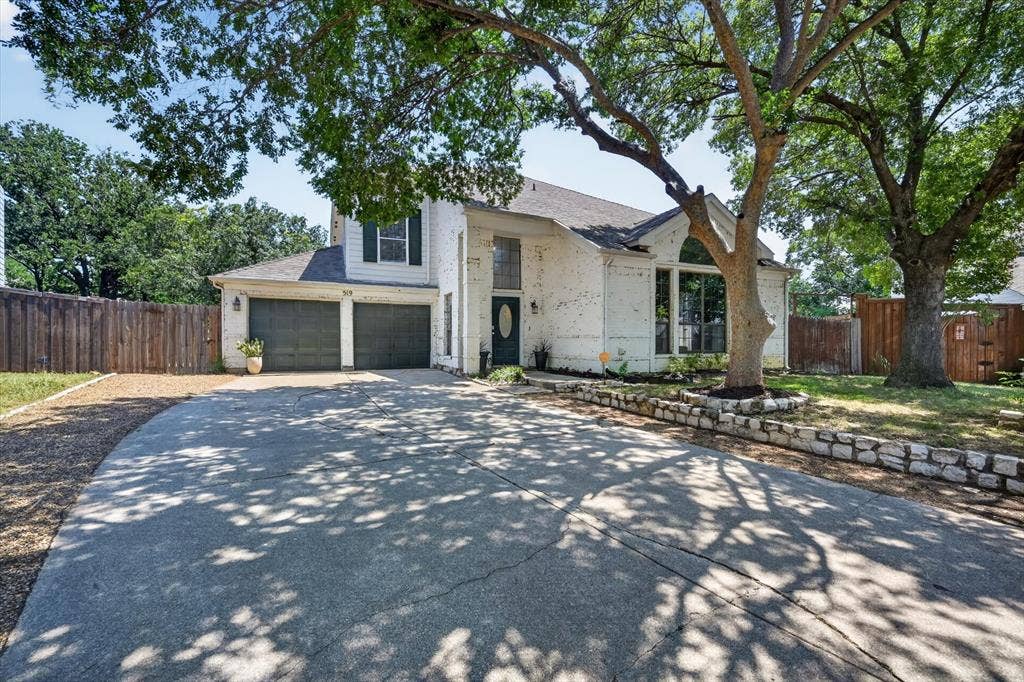 519 Fox Creek Court, Denton, TX 76209 Lime wash brick exterior with a two-car garage, large driveway, arched windows, and a stone retaining wall