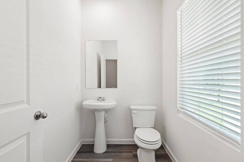 3208 Dillonwood Street, Celina, TX 75009 Guest Bathroom Pedestal sink with chrome faucet, wall-mounted mirror, white toilet, wood-finish flooring, and window with blinds
