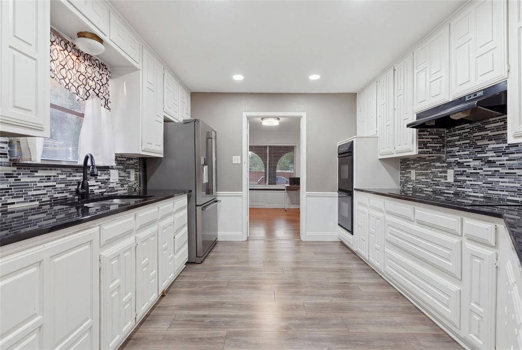 1010 Florence Drive, Duncanville, TX 75116 Galley kitchen featuring white cabinetry, dark countertops, a mosaic tile backsplash, and wood-finish flooring