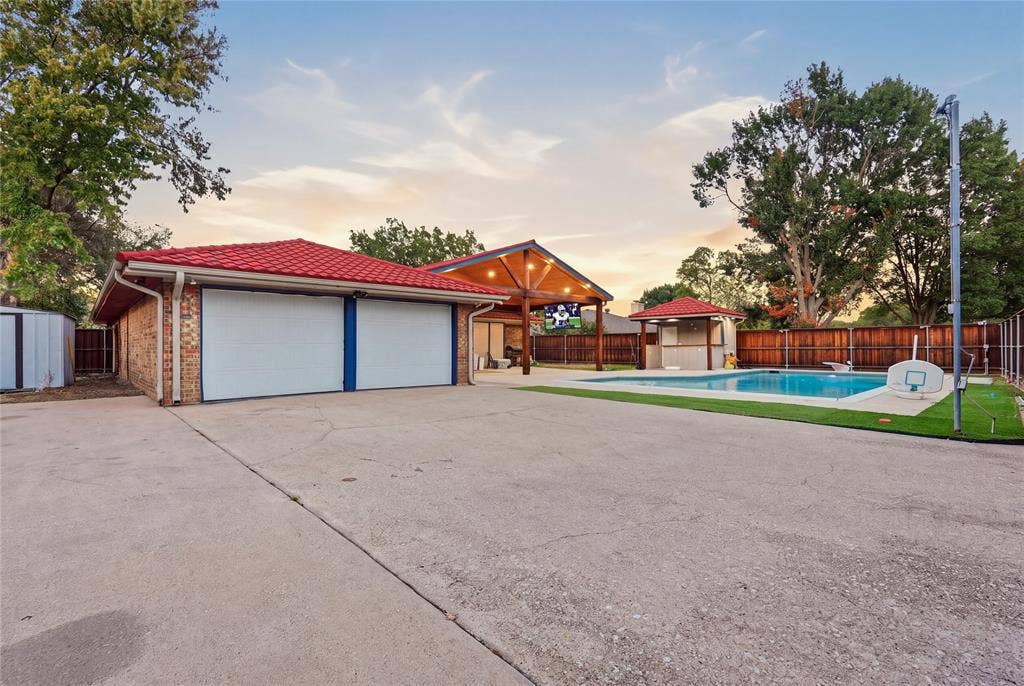1010 Florence Drive, Duncanville, TX 75116 Expansive concrete driveway, two-car garage with white doors, red tile roofing, inground swimming pool, and dedicated outdoor entertaining structure with wood columns