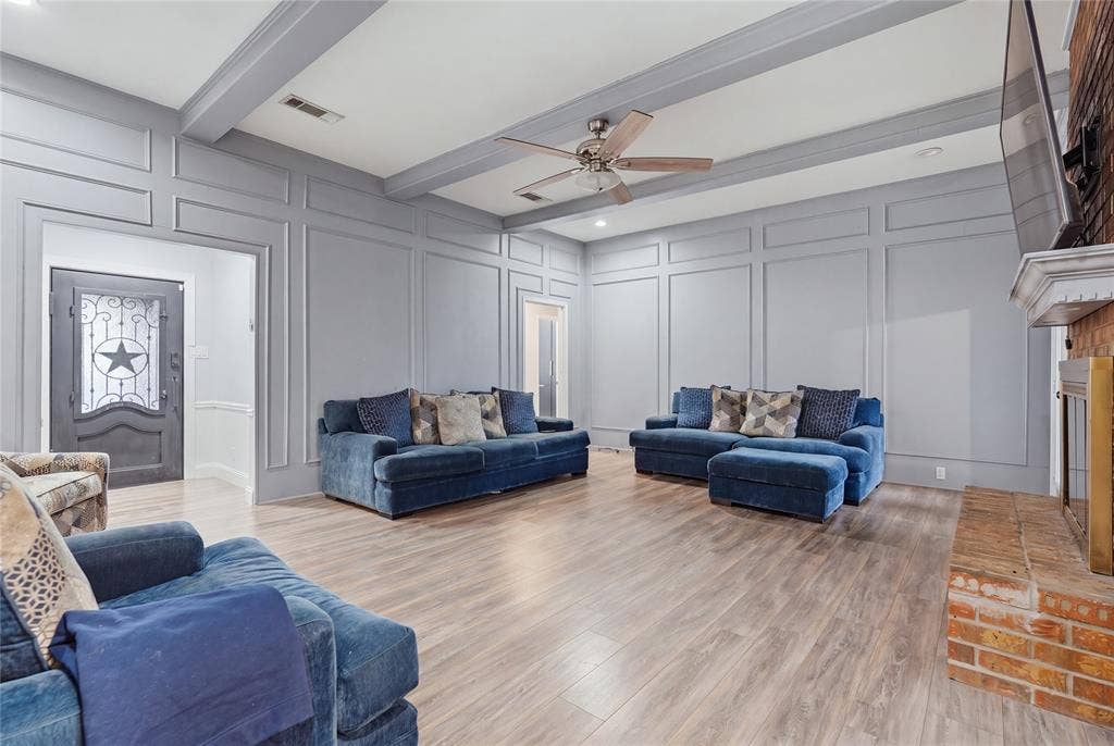 1010 Florence Drive, Duncanville, TX 75116 Wood-finish flooring throughout, tray ceiling with exposed beams, decorative wall paneling, and a brick fireplace